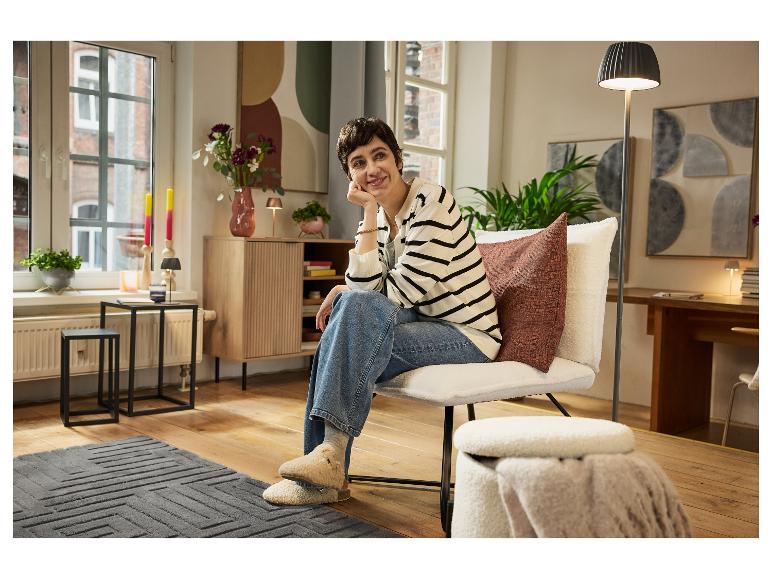 Een vrouw ontspant in een lichte stoel in een modern ingerichte woonkamer.