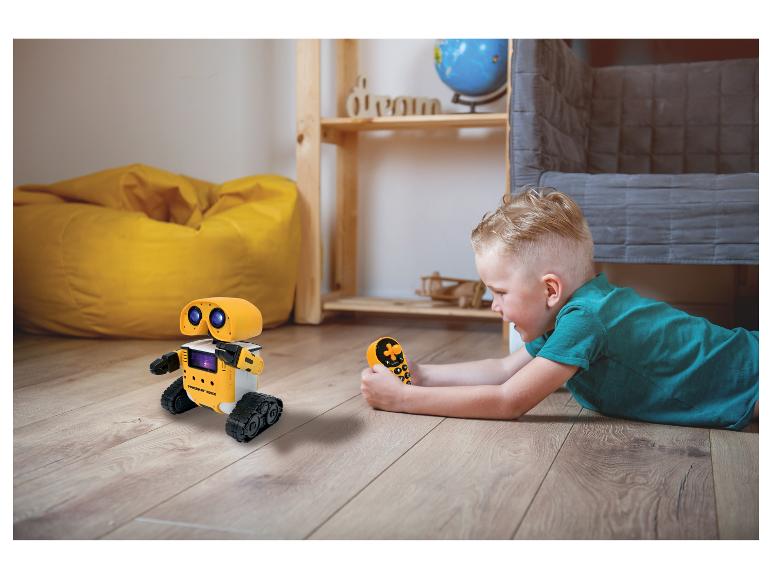 Jongen speelt met gele op afstand bestuurbare robot op de vloer.