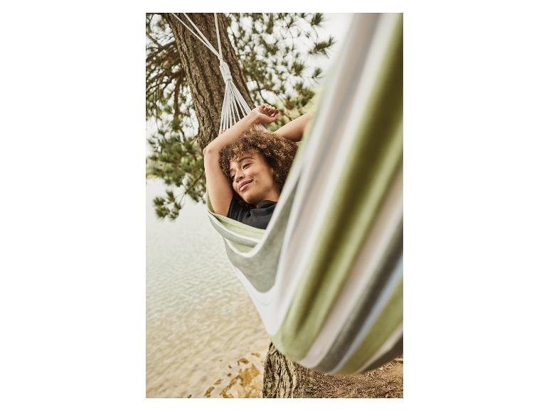 Vrouw ontspannend in een groene en beige gestreepte hangmat bij een meer.