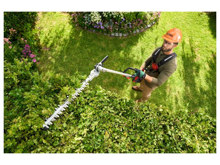 Een man gebruikt een elektrische Parkside heggenschaar om een haag te snoeien.