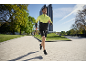 Man in een geel-zwart hardloopjack en zwarte shorts joggend buiten.