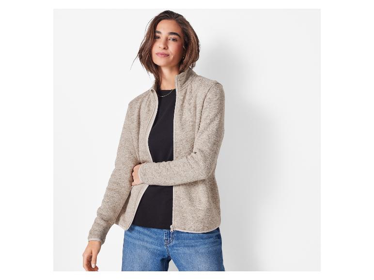 Een vrouw in een beige fleecejack en jeans.