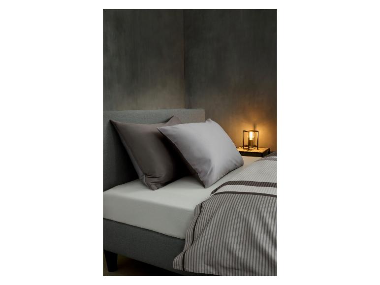 Bed met grijs gestoffeerd hoofdbord, twee kussens en gestreept dekbedovertrek, met lamp.