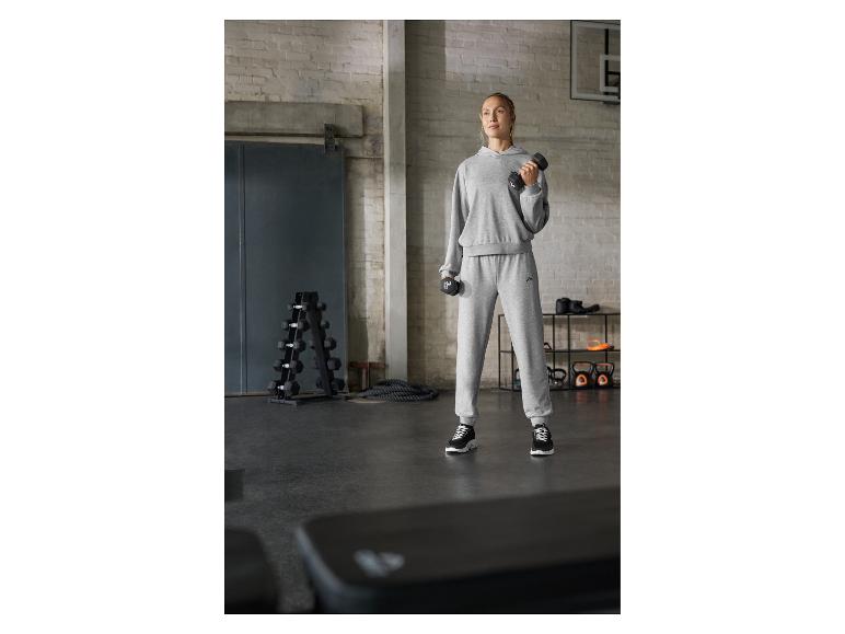 Vrouw in een grijs trainingspak, met halters, in een sportschool.