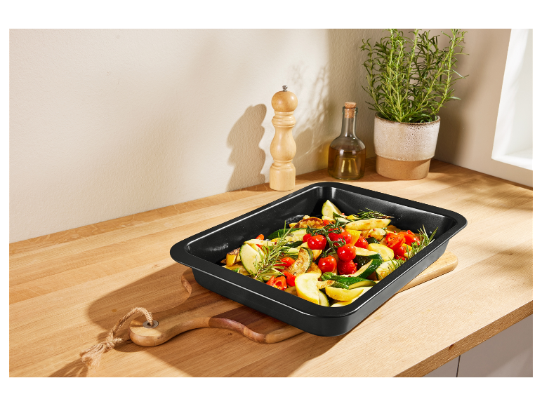 Zwarte bakplaat met geroosterde groenten op een houten aanrecht.