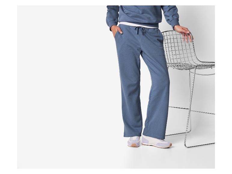 Vrouw in een blauwe loungewear set met witte sneakers, vasthoudend aan een metalen stoel.