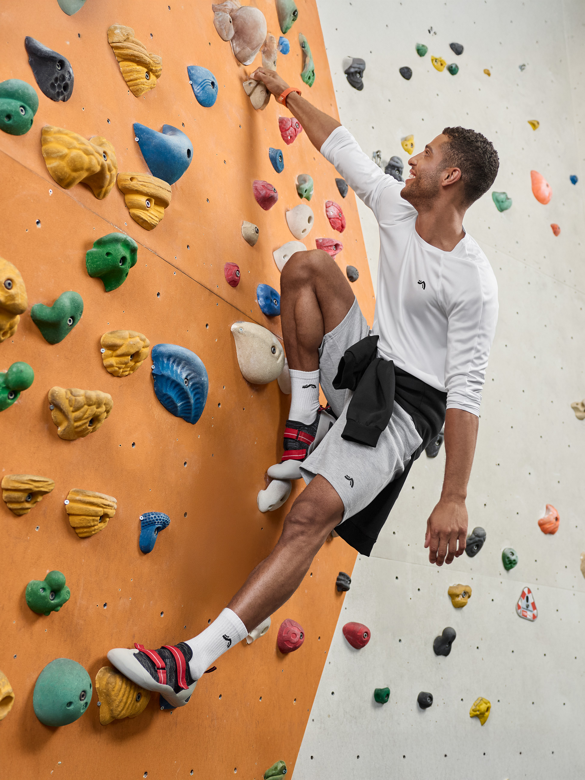 Man in sportkleding klimt op een klimmuur met kleurrijke grepen.