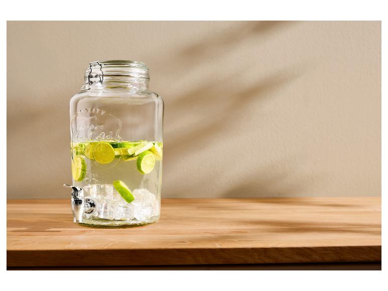 Glazen drankdispenser met kraan, gevuld met water, limoenschijfjes en ijsblokjes.