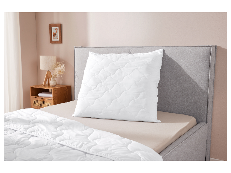 Wit gewatteerd kussen en dekbed op een bed met een grijs hoofdbord