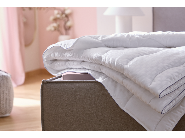 Gevouwen wit dekbed met blauwe bies op een bed in een slaapkamer met roze muren.