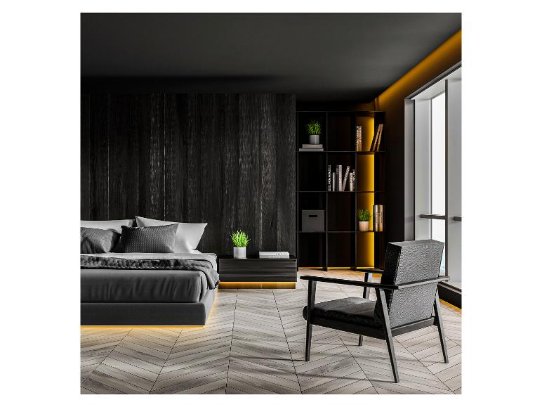 Moderne donkere slaapkamer met bed, fauteuil en boekenkast met decoratieve verlichting.