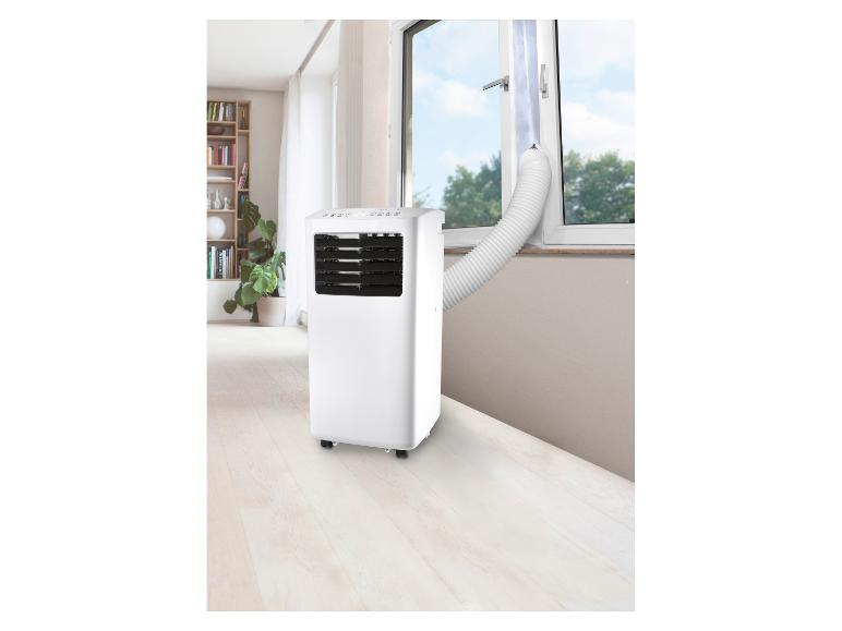 Witte draagbare airconditioner met afvoerslang in een woonkamerraam.