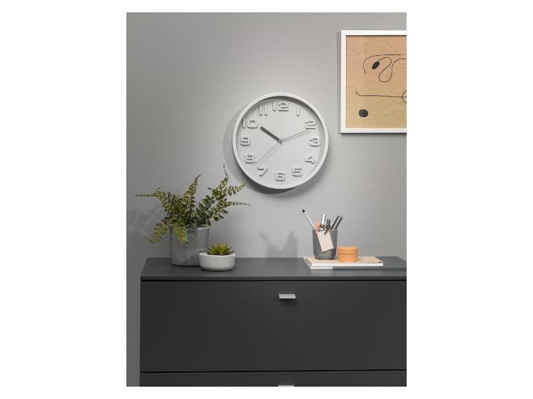 Wandklok, planten en pennenbakje op een grijze kast.