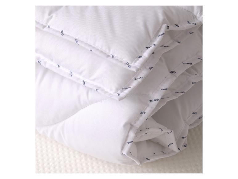 Wit gewatteerd dekbed met een patroonrand, rustend op een getextureerd wit oppervlak.