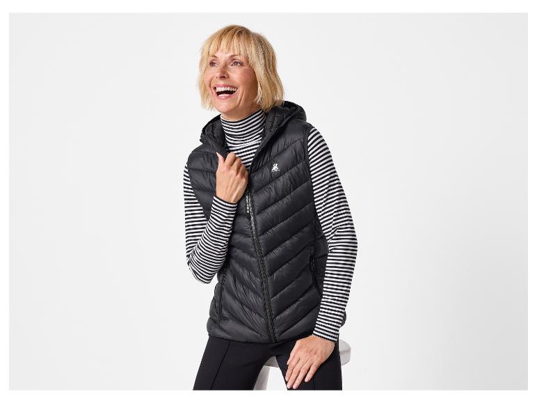 Vrouw in een zwart gewatteerd vest met capuchon en een zwart-wit gestreepte coltrui.