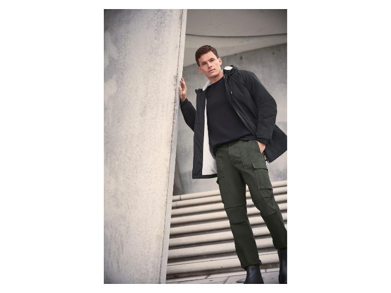 Man in zwarte jas met witte voering, zwart T-shirt en groene cargobroek.