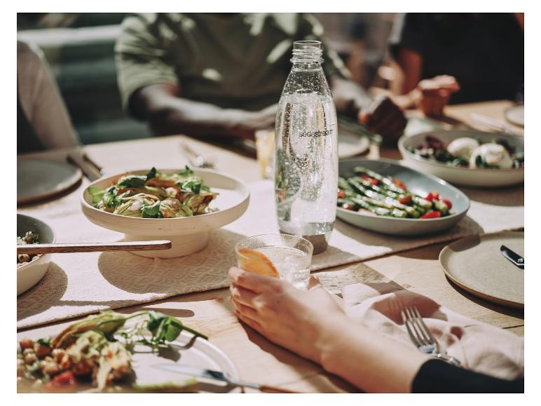 Een Sodastream-fles met bruiswater op een tafel met eten en mensen.