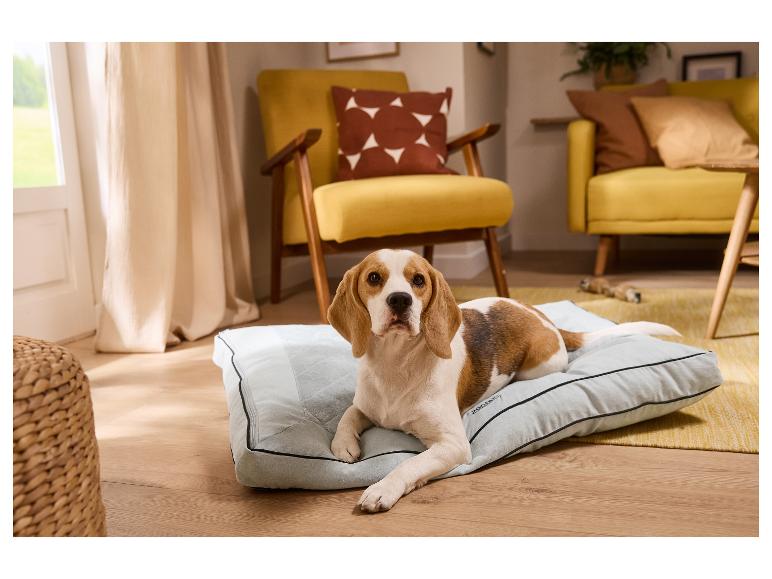 Beagle hond ligt op grijs hondenbed in woonkamer met gele meubels.