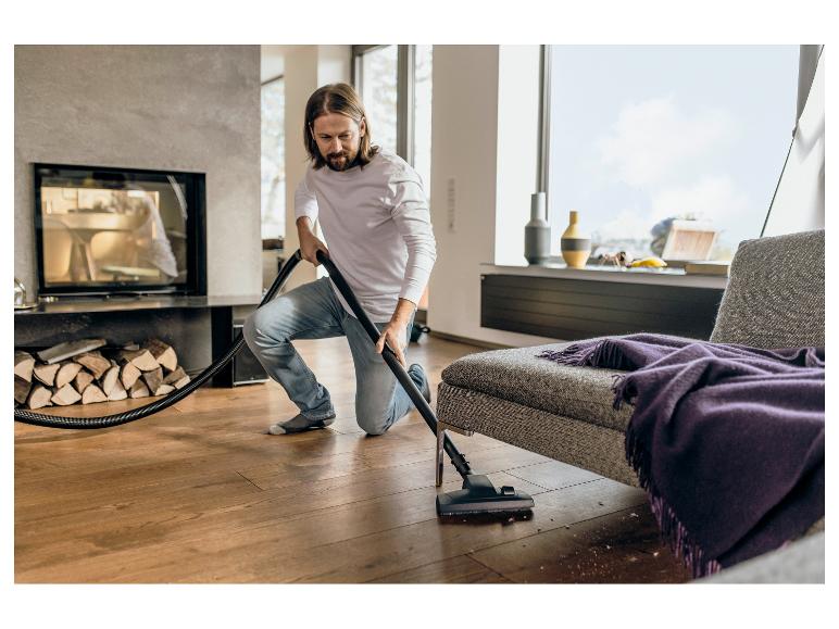 Man stofzuigt houten vloer in moderne woonkamer met open haard.