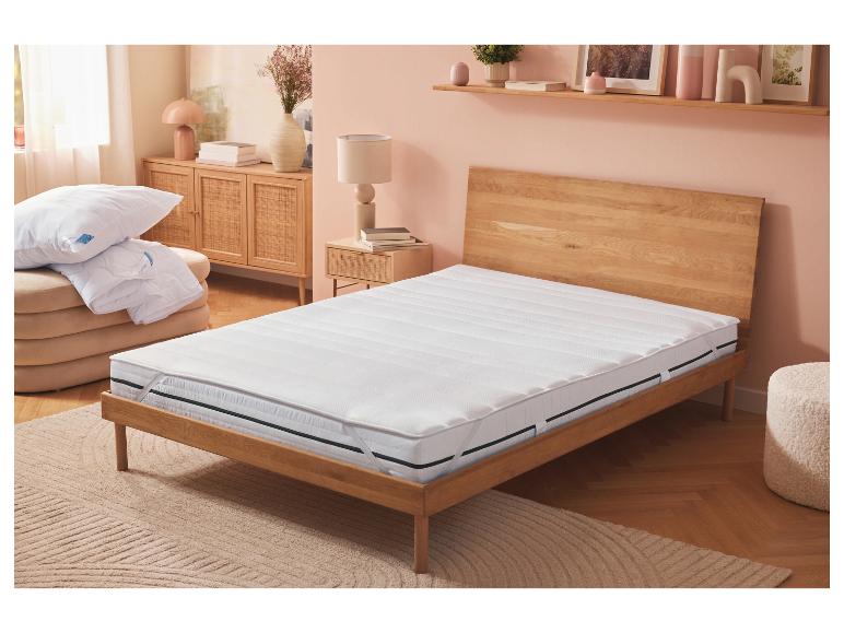 Witte topmatras op een houten bed in een slaapkamer met roze muren.