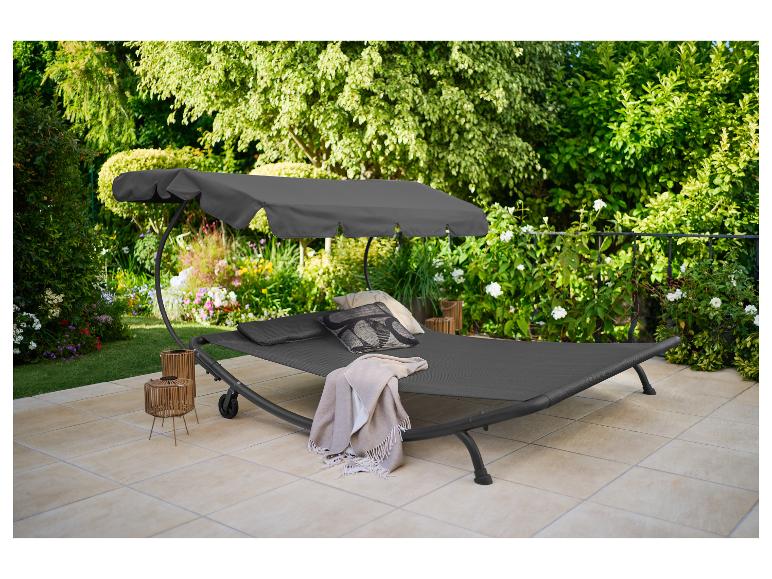 Donkergrijze tuinstoel met luifel, kussens en deken op een terras.