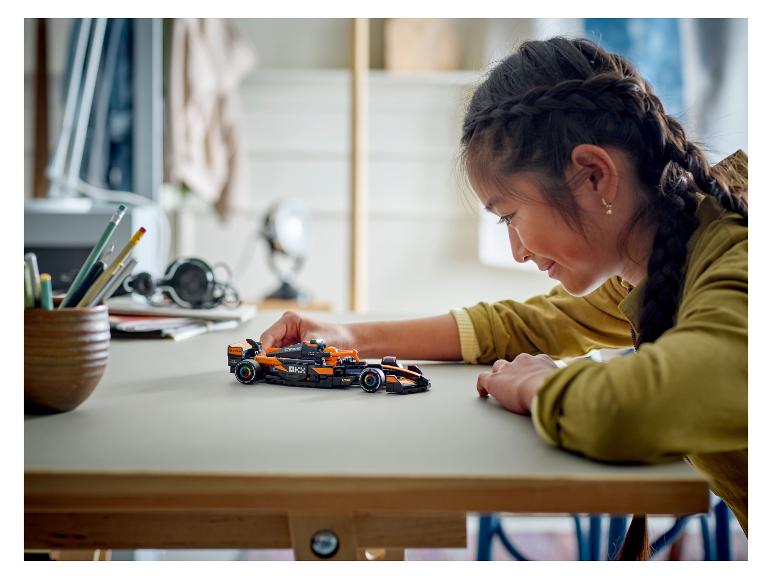 Een meisje kijkt naar een zwart-oranje LEGO Speed Champions McLaren Formule 1-raceauto.