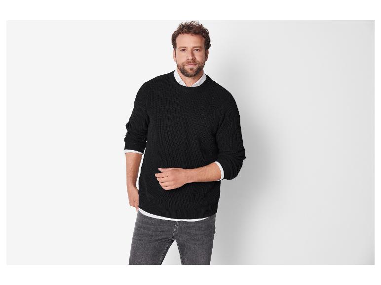 Een man in een zwarte trui en grijze jeans.