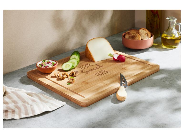 Bamboe snijplank met kaas, groenten en walnoten, naast brood en olie.