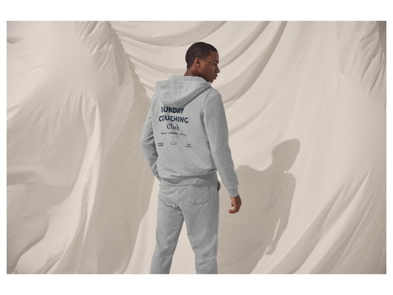 Man in grijze hoodie en joggingbroek met 'Sunday Couching Club'-logo.