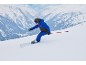 Kind in blauw-zwart skipak, helm en skibril, skiënd op een besneeuwde piste.