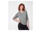 Vrouw met krullend haar in een grijze trui en zwarte jeans.