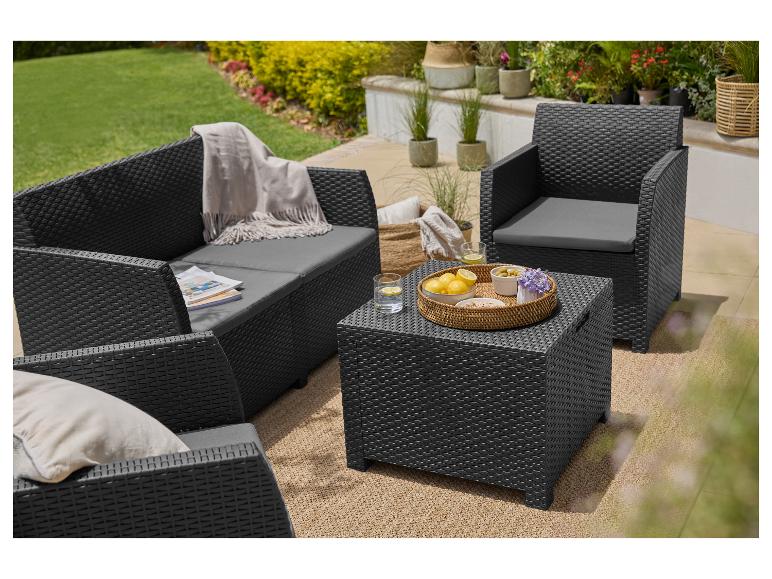 Zwart wicker loungeset met grijze kussens, een salontafel en decoratieve items in een tuin.