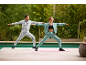 Twee mensen in sportkleding doen yoga buiten bij een zwembad.
