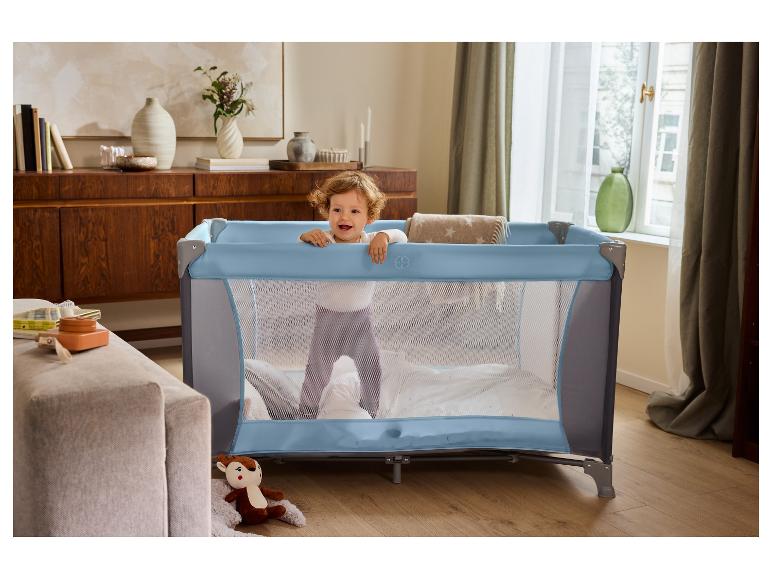 Baby in blauw reisbedje in woonkamer.