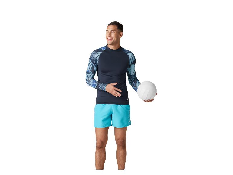 Man in een shirt met lange mouwen en korte broek, met een volleybal.