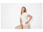 Lachende vrouw in wit geribbeld T-shirt en beige broek, poserend met hand in de zij.