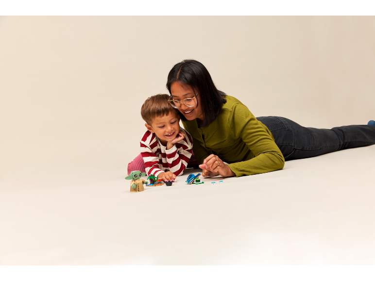 Een vrouw en een kind spelen op de grond met kleine speelgoedfiguren.