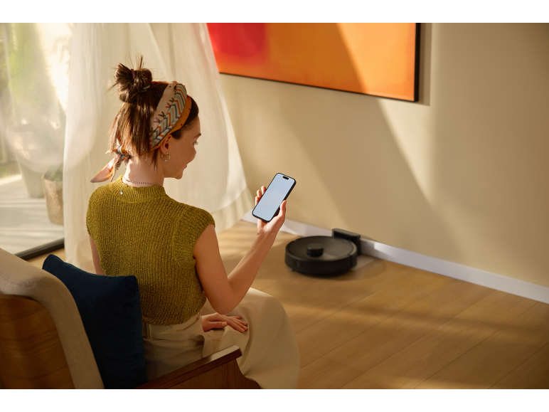 Vrouw bedient robotstofzuiger met smartphone in de woonkamer.