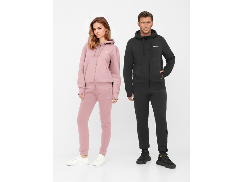 Man en vrouw in hoodies met rits en joggingbroek, vrouw in roze, man in zwart.