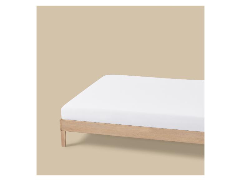 Wit hoeslaken op een houten bedframe tegen een beige achtergrond.