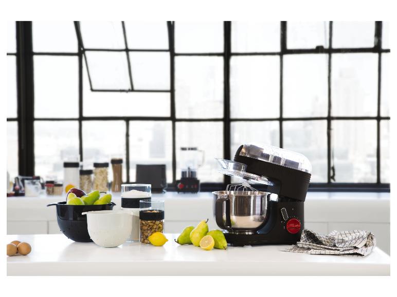 Keukenmachine en keukengerei op een wit aanrecht voor een raam.