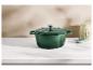 Groene gietijzeren braadpan op een wit aanrecht met een decoratieve pot en een kommetje.