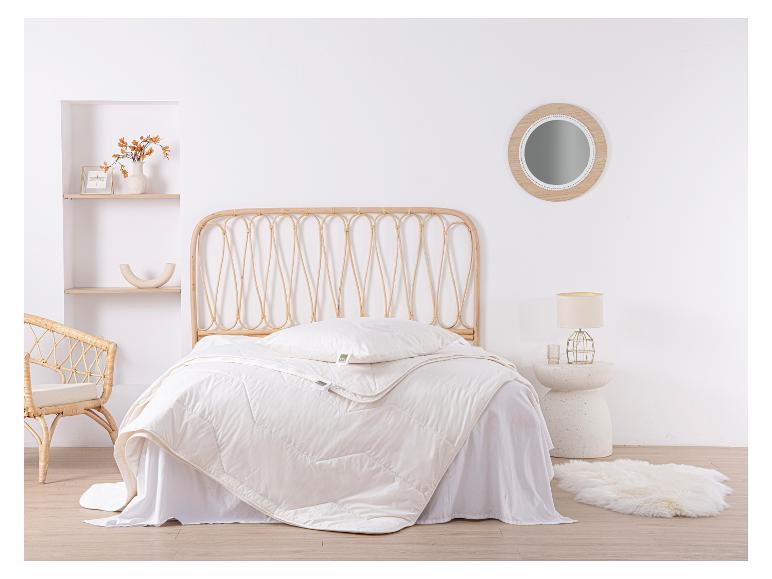 Slaapkamer met rotan hoofdbord, wit dekbed en kussen met TXL-label.