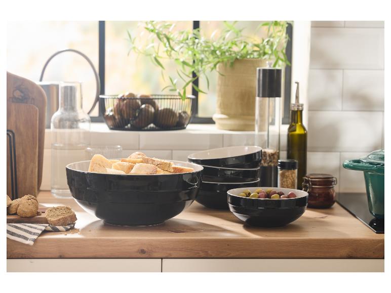 Zwarte keramische kommen met brood en olijven op een houten aanrecht.