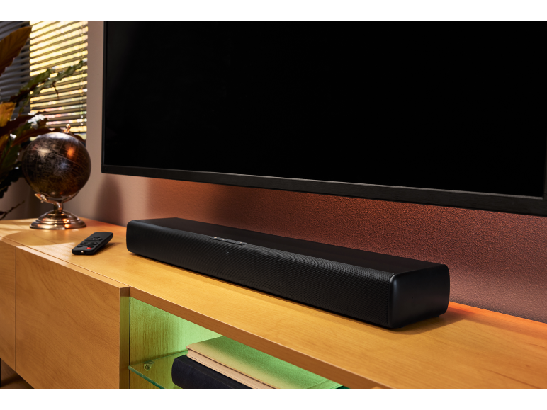 Zwarte soundbar onder een televisie, met afstandsbediening en globe op een houten meubel.