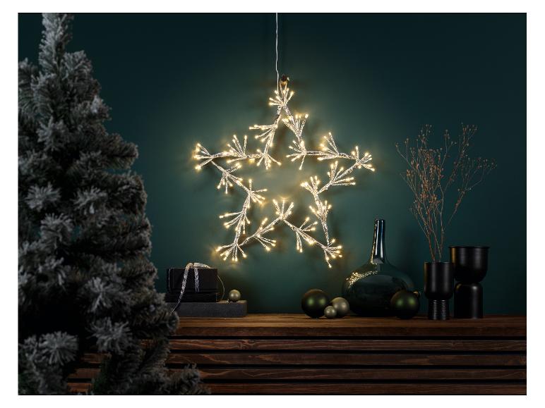 Een verlichte sterdecoratie aan een donkergroene muur boven een houten oppervlak met kerstdecoratie.