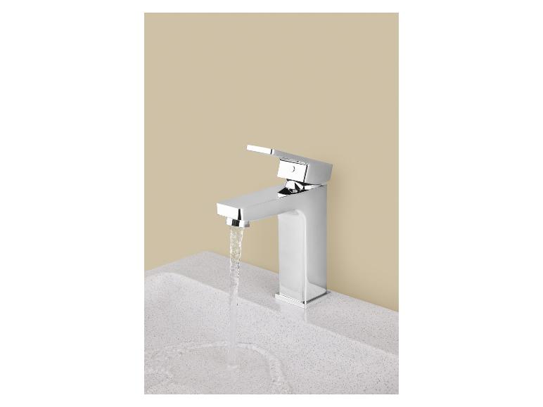 Moderne chromen kraan met stromend water in een witte wastafel.