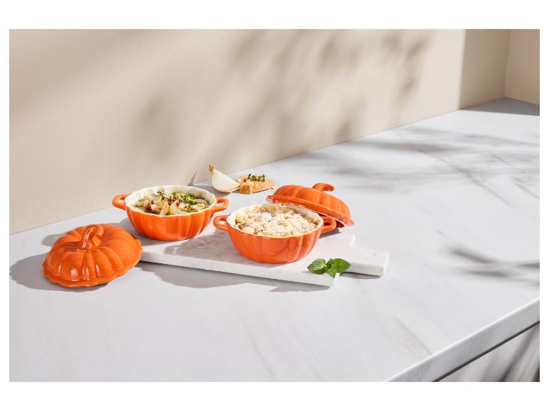 Twee oranje pompoenvormige ovenschalen met eten op een marmeren ondergrond.
