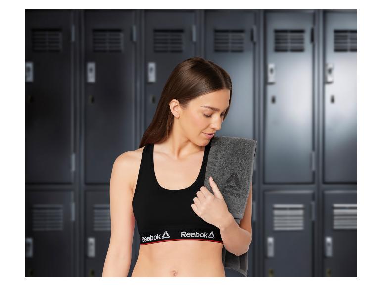 Vrouw in Reebok sportbeha, met een grijze handdoek in de kleedkamer.