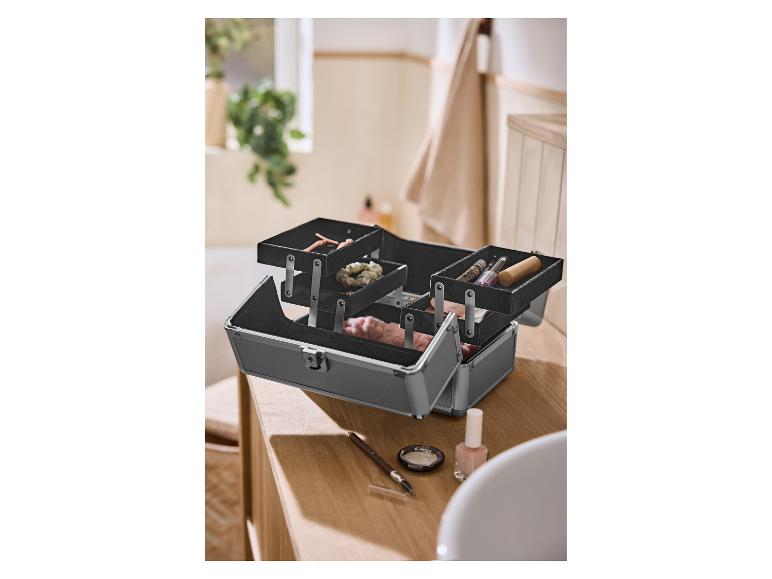 Open zwarte make-upkoffer met cosmetica en accessoires op een houten aanrecht.